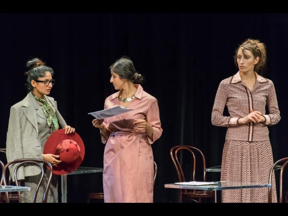 Three women in An Enemy of the People standing around a document during the Ballerup production.