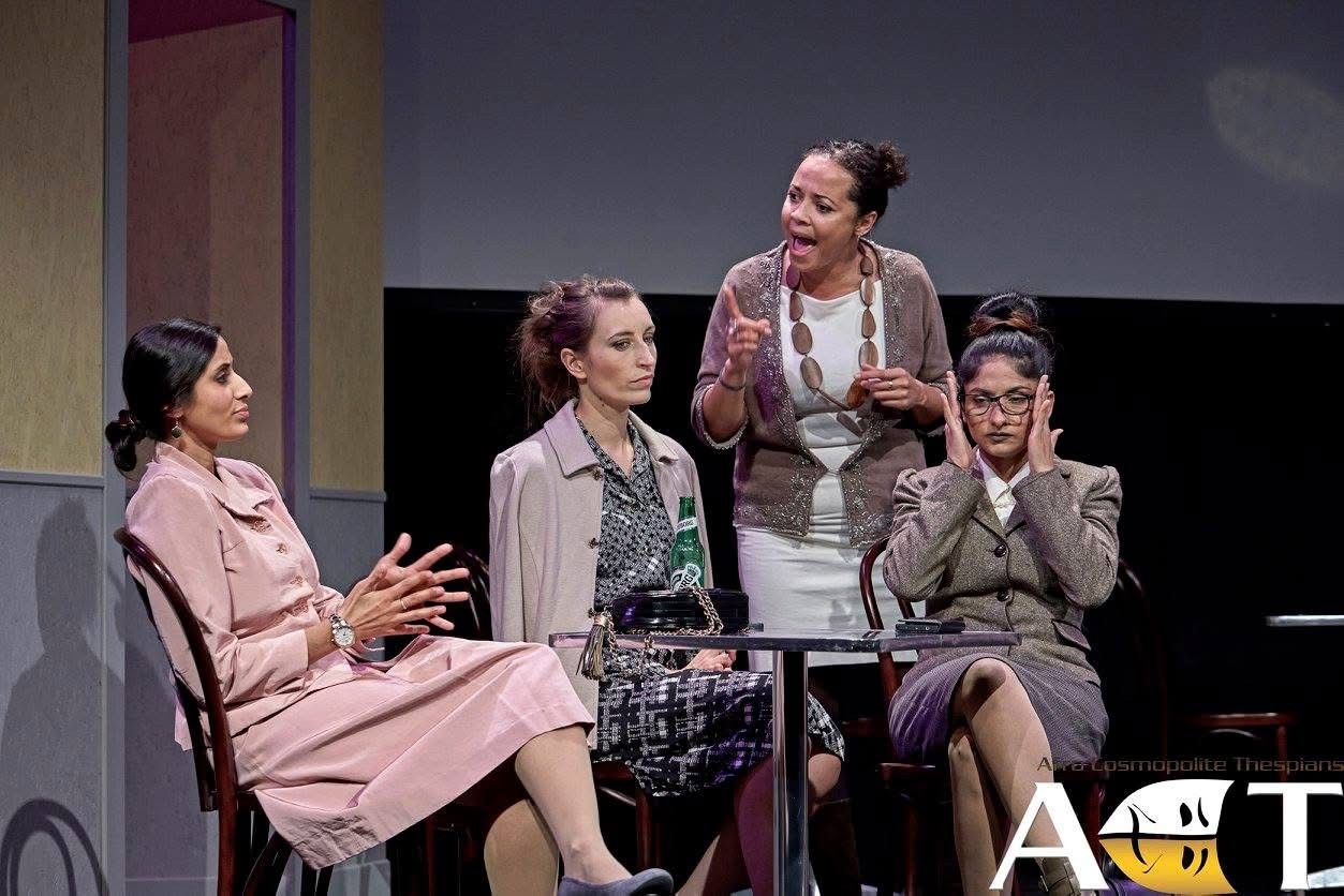 A public-room scene from An Enemy of the People with four women seated and standing around a table.