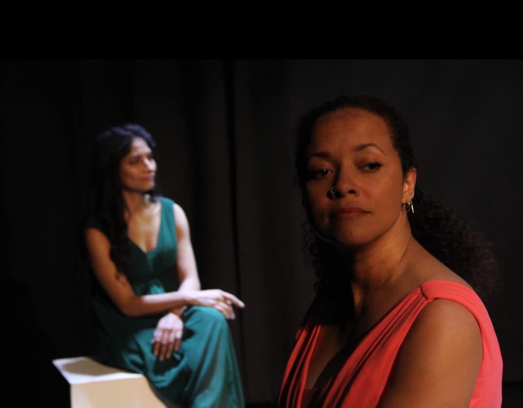 Two women in a moody red and green stage composition.